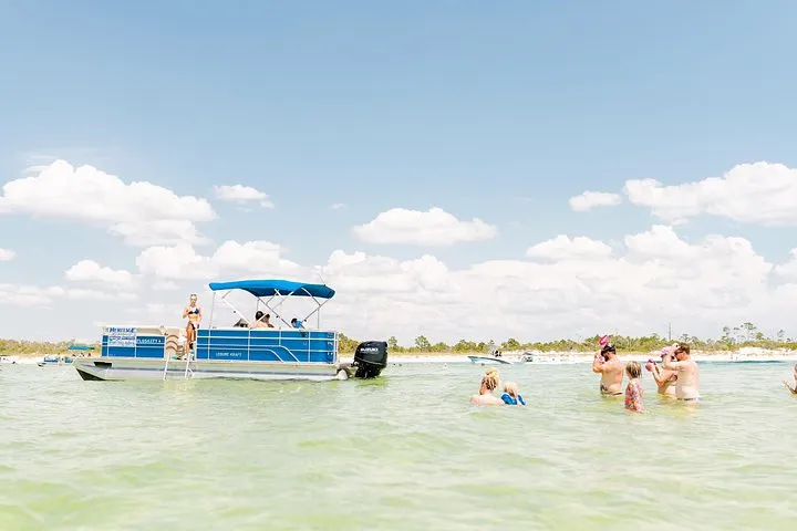 A pontoon with a blue bimini top in shallow water with swimmers on a Shell Island pontoon rental from Panama City Beach, Florida