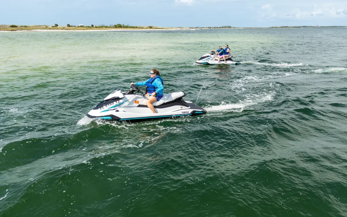 Riders on rental jet skis crossing green water in Panama City Beach, the ride on a Shell Island jet ski dolphin tour in Florida